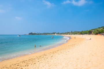 At the beach of one of the major tourist spots in the south west of Sri Lanka. Tourist do sunbathing and aquatic sports. Outrigger and traditional fishing boats on the beach