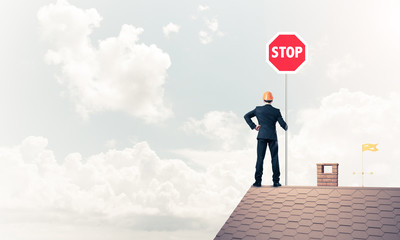 Caucasian businessman on brick house roof showing stop road sign