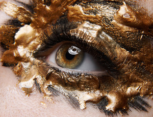 Macro and close-up creative make-up theme: beautiful female eye with golden black paint, retouched photo