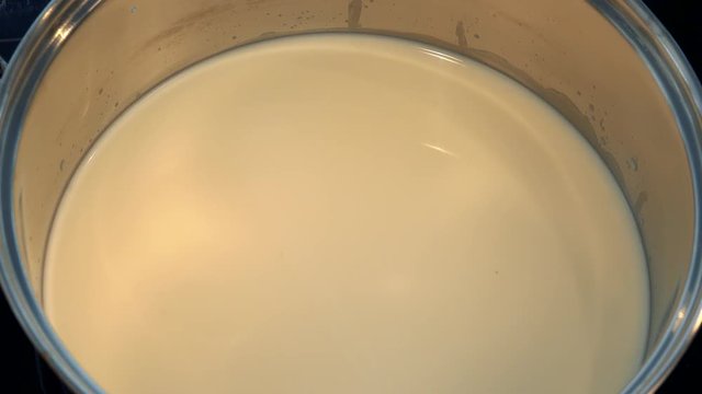 A woman takes a cover off a pot of milk - closeup from above