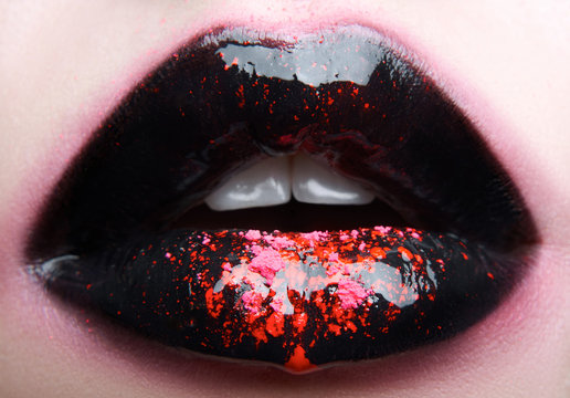 Macro and close-up creative make-up theme: Beautiful plump female lips with black and pink paint, wet effect on the lips