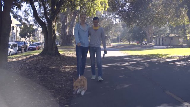 Happy Gay Couple Walk Their Corgi Dog On Path Through A Park In San Francisco 