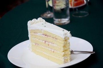 Slice of sponge cake with cream and strawberry jam, decorating with eatable silver balls, on the plate