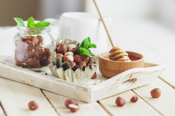 Honey in the wooden bowl, mint leaves, hazelnuts and jar with milk on the wooden tray