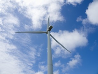 Fototapeta premium Wind turbine on the sky background, close up, bottom-up viewTop part of the wind turbine on the background of the blue sky, partly covered with white clouds, bottom-up view