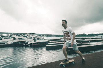 A man with a skateboard in a yacht club near the river