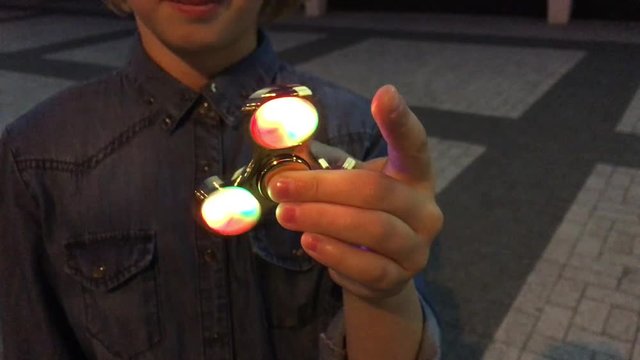 Cheerful school girl playing with a luminous fidget spinner, evening outdoors. A popular trendy toy.