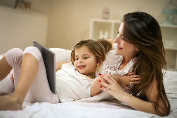 Smiling mother with daughter using digital tablet on bed.