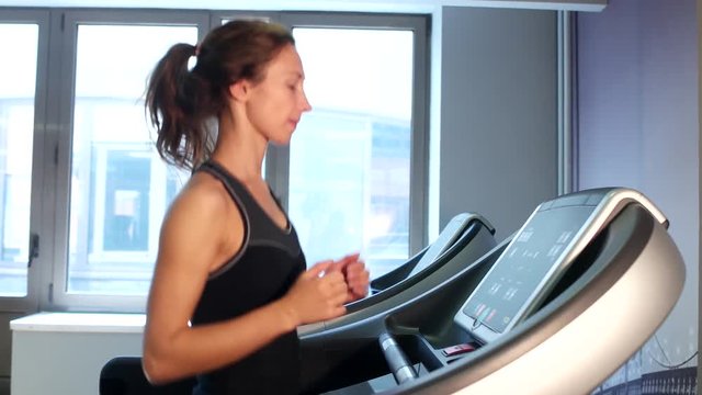 A beautiful brunette girl is running on the treadmill