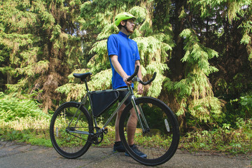 Cyclist with green helmet on a mountain road in forest. Black bicycle