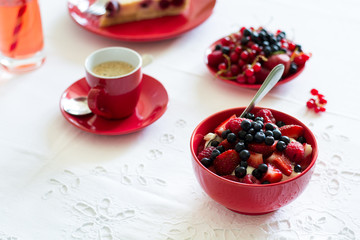 Healthy breakfast: cottage cheese with sour cream, strawberry, raspberry and blueberry, espresso, cherry cheesecake and plate of fresh ripe berries on white table cloth. Selective focus