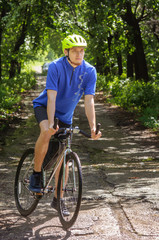 Obraz premium Cyclist with green helmet on a mountain road in forest. Black bicycle