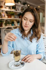 A young woman sits in a cozy light kitchen at the table and makes herself a tea