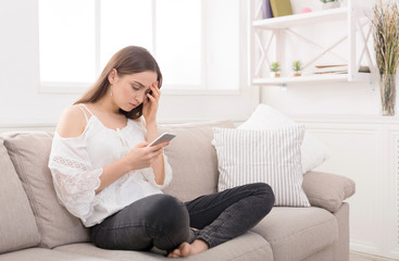 Obraz premium Young anxious woman messaging on smartphone