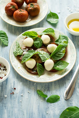 Plate of fresh caprese salad with black tomatoes, mini mozzarella and basil leaves on blue wooden table. Selective focus