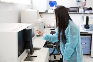 Laboratory assistant loading sample tubes for coagulation test analysis and inputing data to coagulation machine