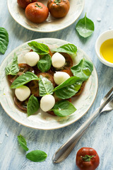 Obraz na płótnie Canvas Plate of fresh caprese salad with black tomatoes, mini mozzarella and basil leaves on blue wooden table. Selective focus