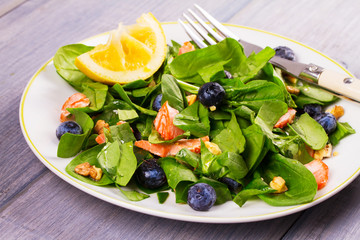 Salmon, spinach, blueberries and walnuts salad on white plate