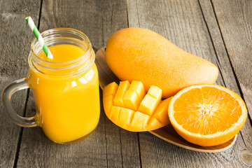 Naklejka na ściany i meble Mango and orange juice and slice of orange on wooden table. Fresh healthy tropical drink.
