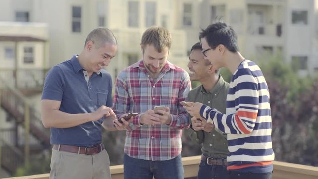 Group Of Happy Gay Friends Check Their Smart Phones And Share Photos With Each Other At A Rooftop Party In San Francisco 
