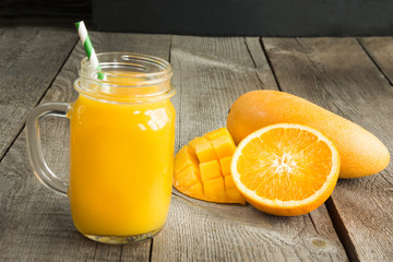 Plakat Mango and orange juice and slice of orange on wooden table. Fresh healthy tropical drink.