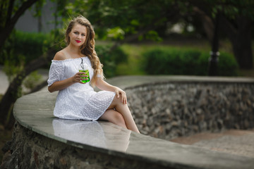 Portrait of a young beautiful attractive woman outdoors in the summer with a glass of ice-cold juice or drink. Pretty girl outside with fresh drink