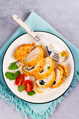Chicken Kiev garnished with tomato and cilantro. Breaded chicken breast stuffed with herbs and butter on white plate. View from above, top studio shot.