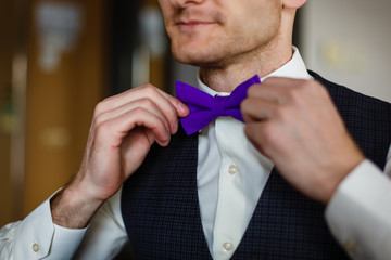 butterfly of violet color on a neck at the man. Man wears purple, purple bow-tie. The bridegroom going to the wedding. Wedding morning. The man straightens his tie.
