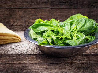 Spinach leaves in bowl on wooden background