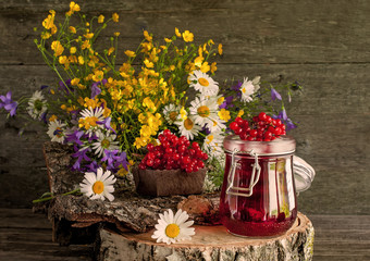 The juice from the berries of viburnum in glass containers on a napkin next to a bouquet of wild flowers on a wooden stand. Rustic.