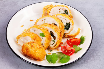 Chicken Kiev garnished with tomato and cilantro. Breaded chicken breast stuffed with herbs and butter on white plate