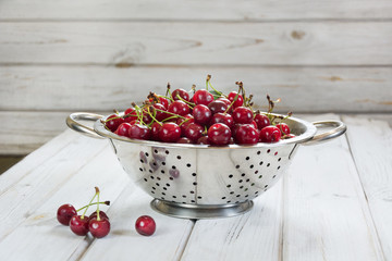 Metal strainer or bowl with ripe berries and cherry on wooden background. Colander filled with fresh cherries over a rustic board.