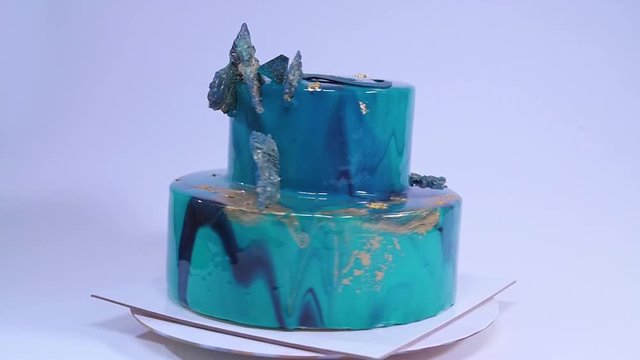 Mousse cake decorated in marine style covered with blue mirror glaze and white chocolate seashells. European french dessert.