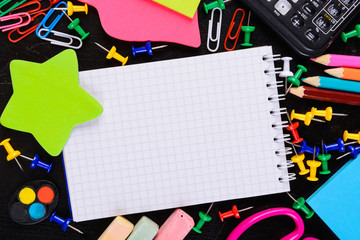 School tools with empty notebook in center with copy space over black background