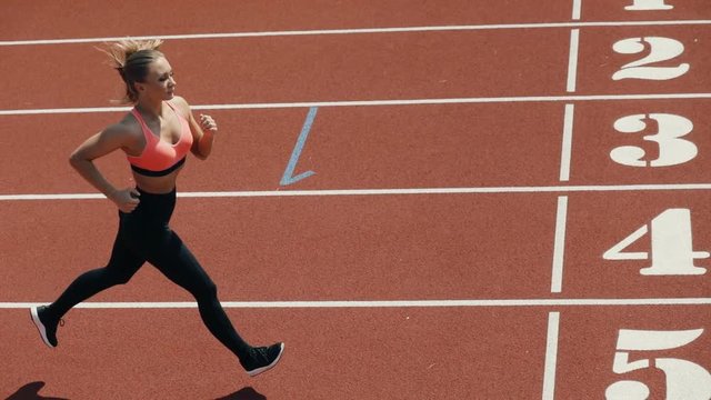 Young adult sport woman sprinter athlete running on stadium track in slow motion