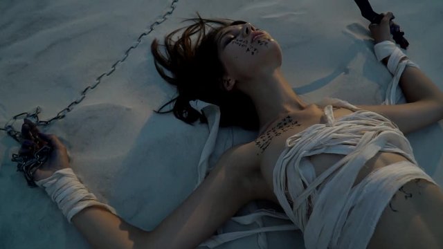 A tranquil woman mummy lies on the sand, holds a chain and a dagger in her hands