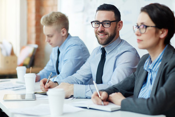 Happy leader looking at camera whilemaking notes at conference or seminar