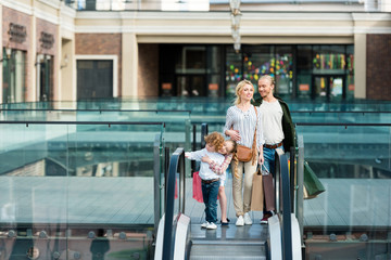 Happy young family holding shopping bags while standing together on escalator