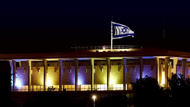 Knesset building the Parliament of Israel with flying waving flag of Israel at night. The Knesset located in Jerusalem and elects both President and Prime Minister and supervises Israeli government