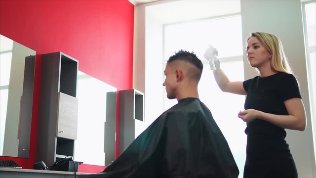 A young and professional hair stylist who works in a hair salon sprinkles water from an atomizer on the visitor's hair in order to make a fashionable hairstyle.