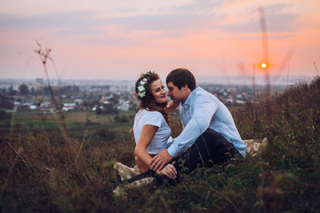 couple, love, nature and people concept - happy loving couple sitting on a plaid in a field on a background of magical sunset