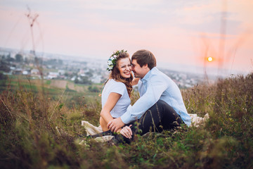 couple, love, nature and people concept - happy loving couple sitting on a plaid in a field on a background of magical sunset