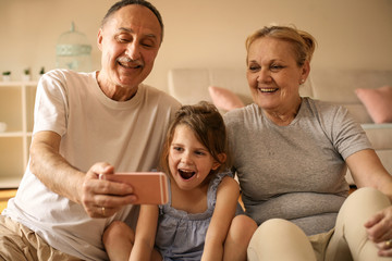 Grandmother and grandfather with their granddaughter using smart phone.