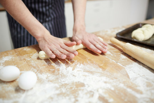 Baker rolling dough for buns on wooden board