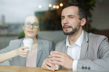 Two co-workers with drinks looking through cafe window