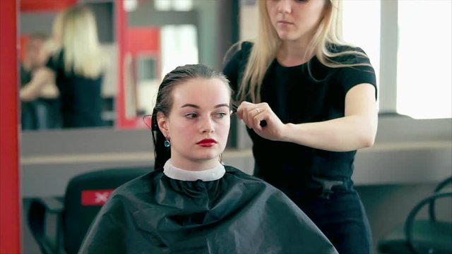 A young and experienced hair stylist who goes through the practice in a beauty salon combs his wet hair in order to dry his hair with a hairdryer and make stylish curls.