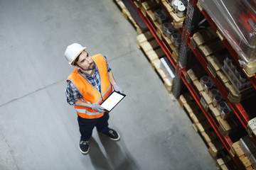 Dispatcher in helmet and uniform making inventory in storehouse