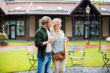 casual couple drinking coffee while standing together at park near buildings