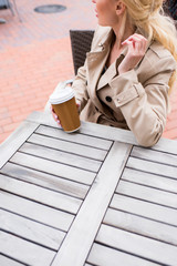 cropped shot of young woman drinking disposable coffee while sitting at cafe on the street