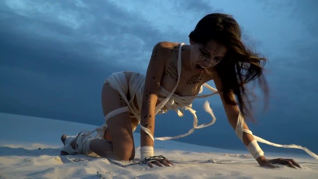 A woman mummy kneels in the sand and screams